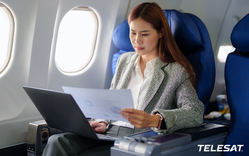 Business woman sitting in seat on plane while working on her laptop