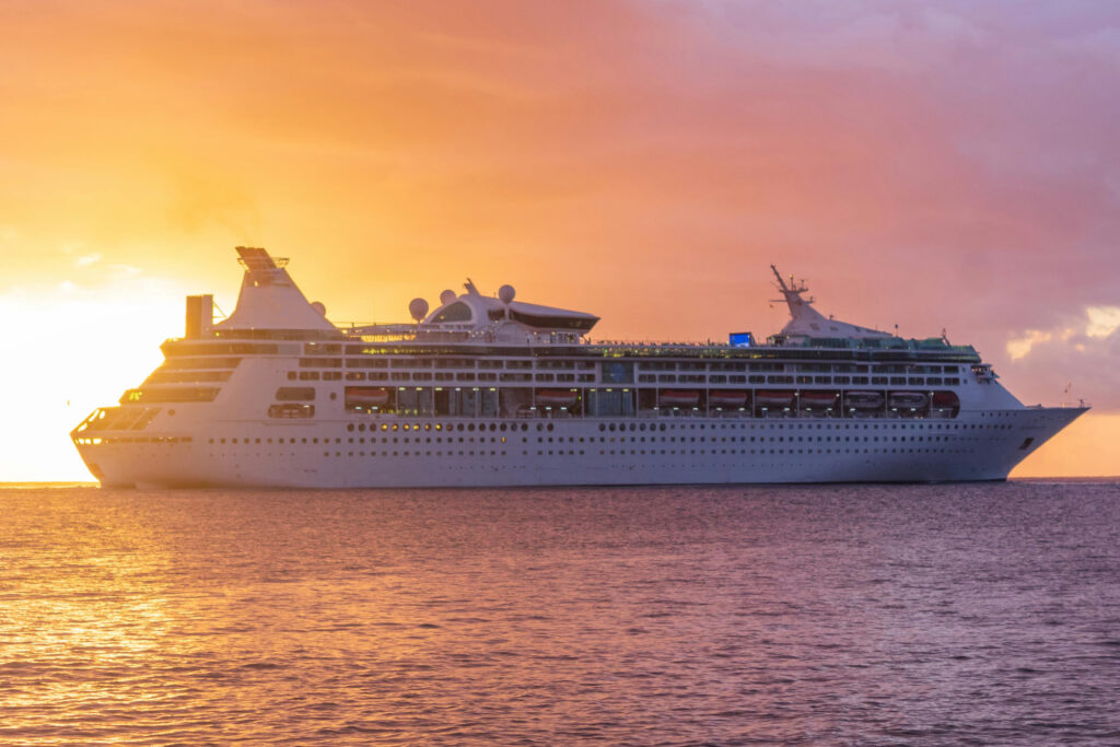 large cruise ship on ocean with sun setting behind