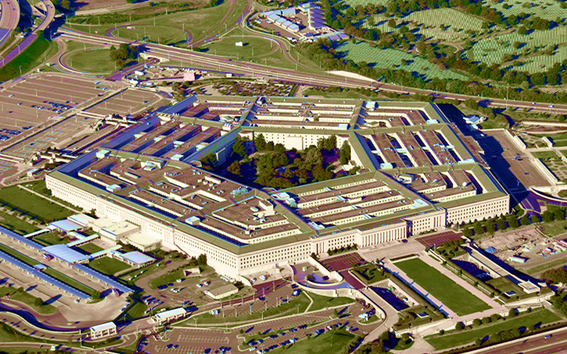 An image of Pentagon buildings captured from the bird view. We can see brown roof tops and green fields around.