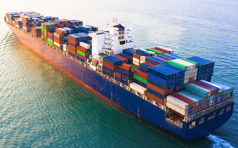 A cargo ship in the sea carrying a pile of shipping containers. The majority of colors are blue and red.