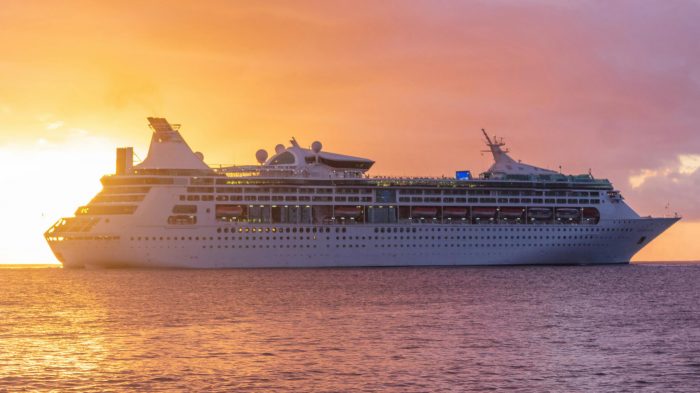 large cruise ship on ocean with sun setting behind