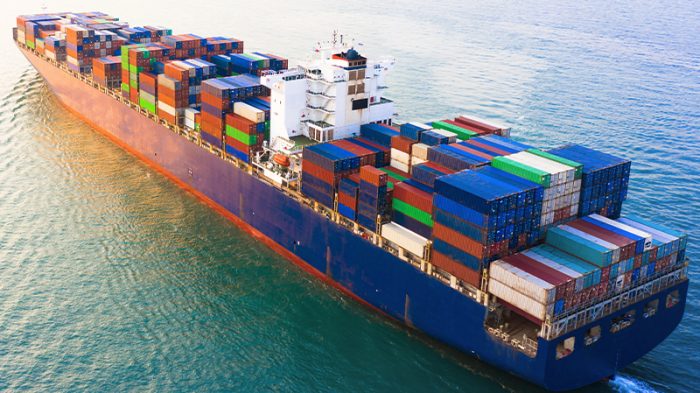 A cargo ship in the sea carrying a pile of shipping containers. The majority of colors are blue and red.